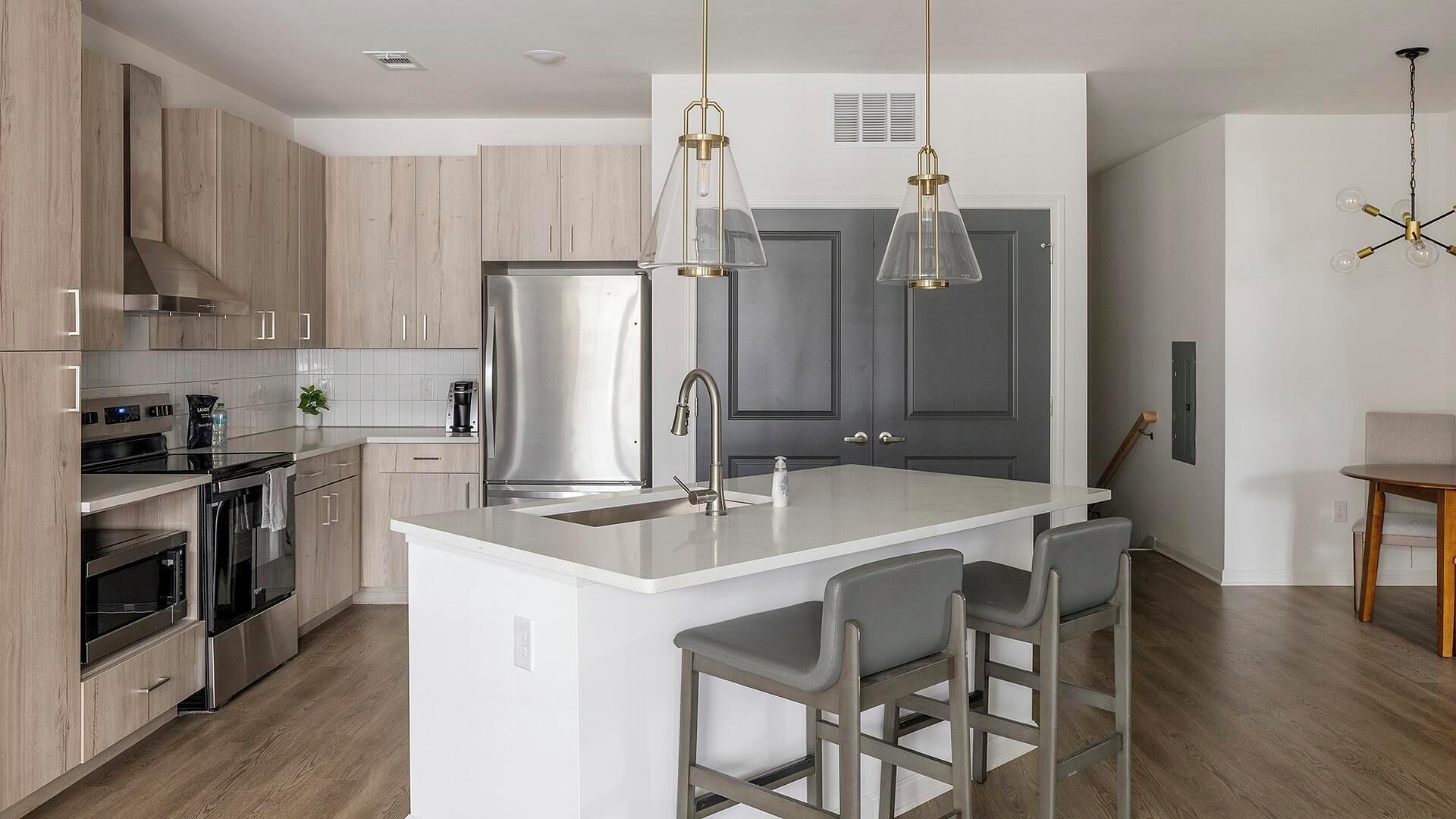 A modern kitchen with stainless steel appliances, a white island with bar stools, and pendant lighting.