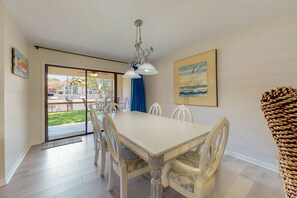 A dining area with a white table and chairs, a chandelier, a painting, and a view through a glass door. - Exclusive 2BR tennis condo with beach access (Miramar Beach)