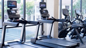 En rad löpband med digitala skärmar, placerade i ett gym med stora fönster.