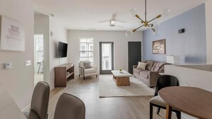 En moderne stue med et fladskærms-tv, en loftventilator, et spiseområde med bord og stole samt en sofa.