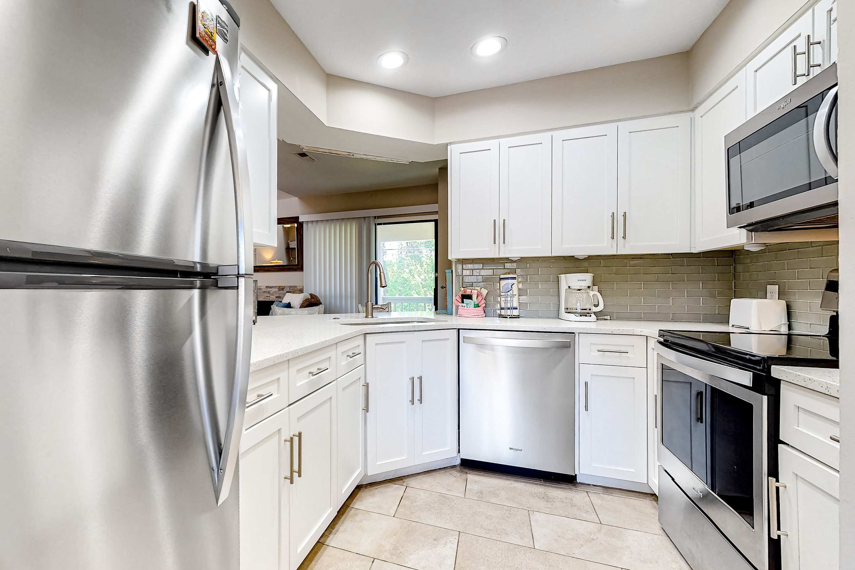 A modern kitchen with stainless steel appliances, white cabinetry, and a tiled backsplash.