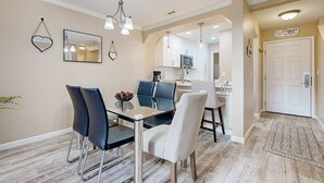 Uma sala de jantar com mesa de vidro, cadeiras e luminárias pendentes.