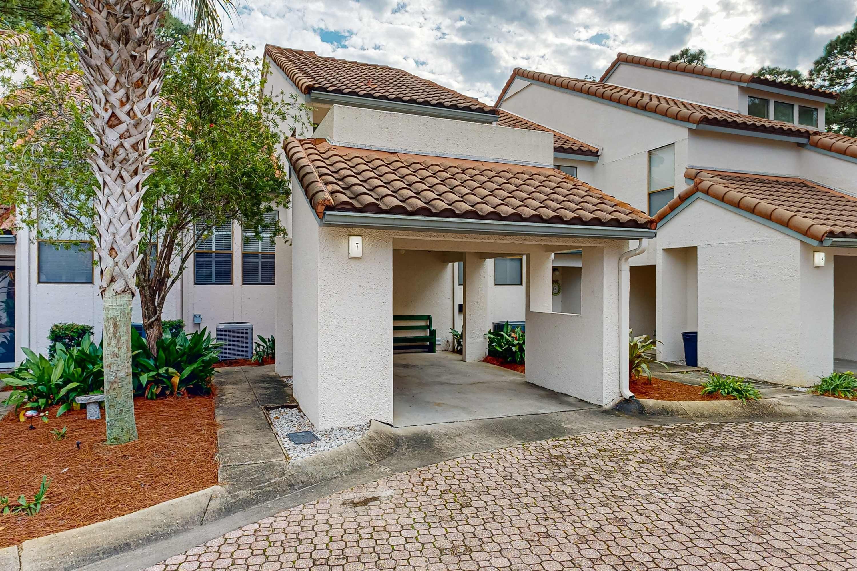A residential building with a tiled roof, a covered driveway, and a landscaped garden.