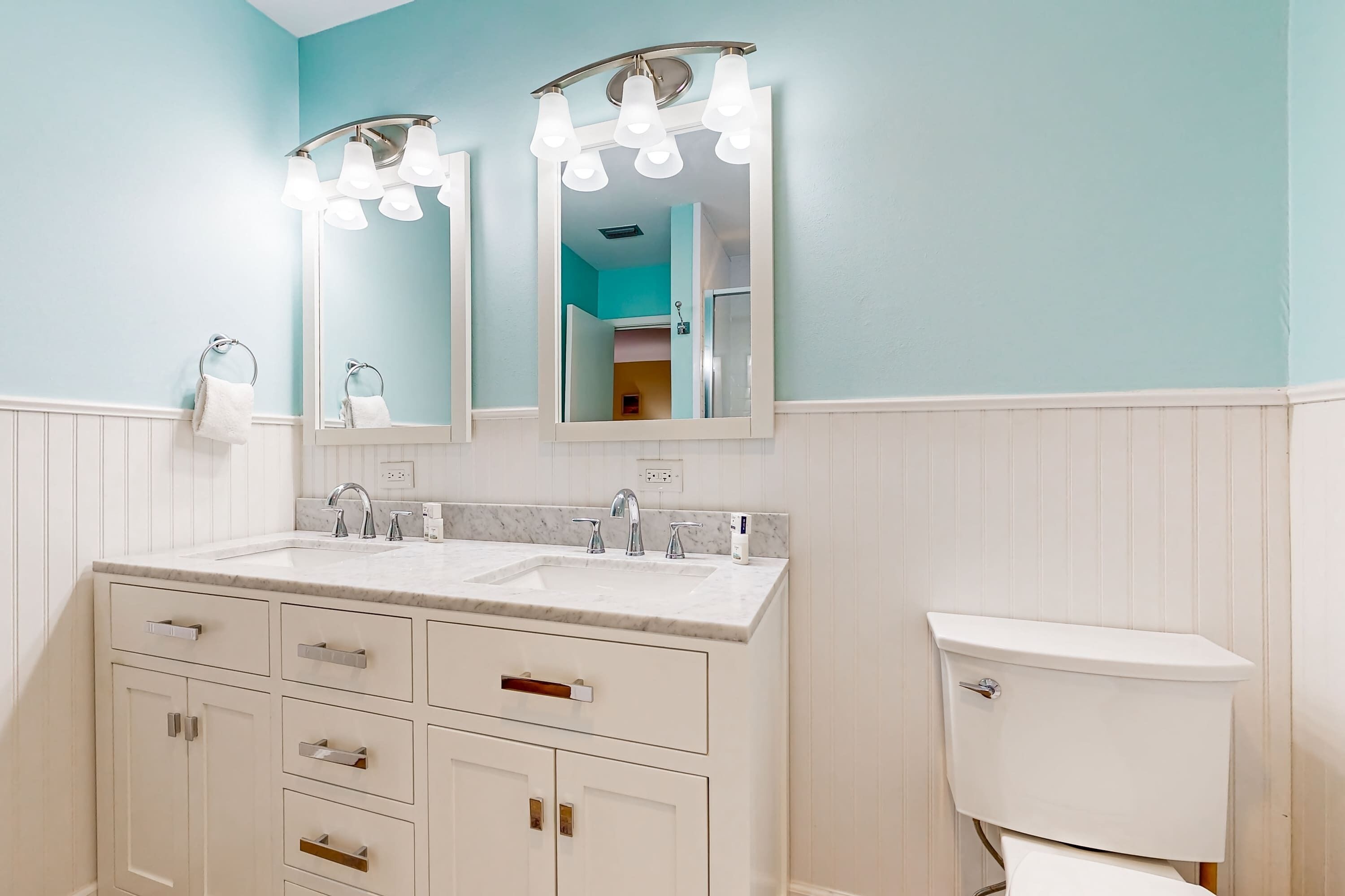 A bathroom with a double sink vanity, a toilet, and two wall-mounted mirrors with light fixtures.