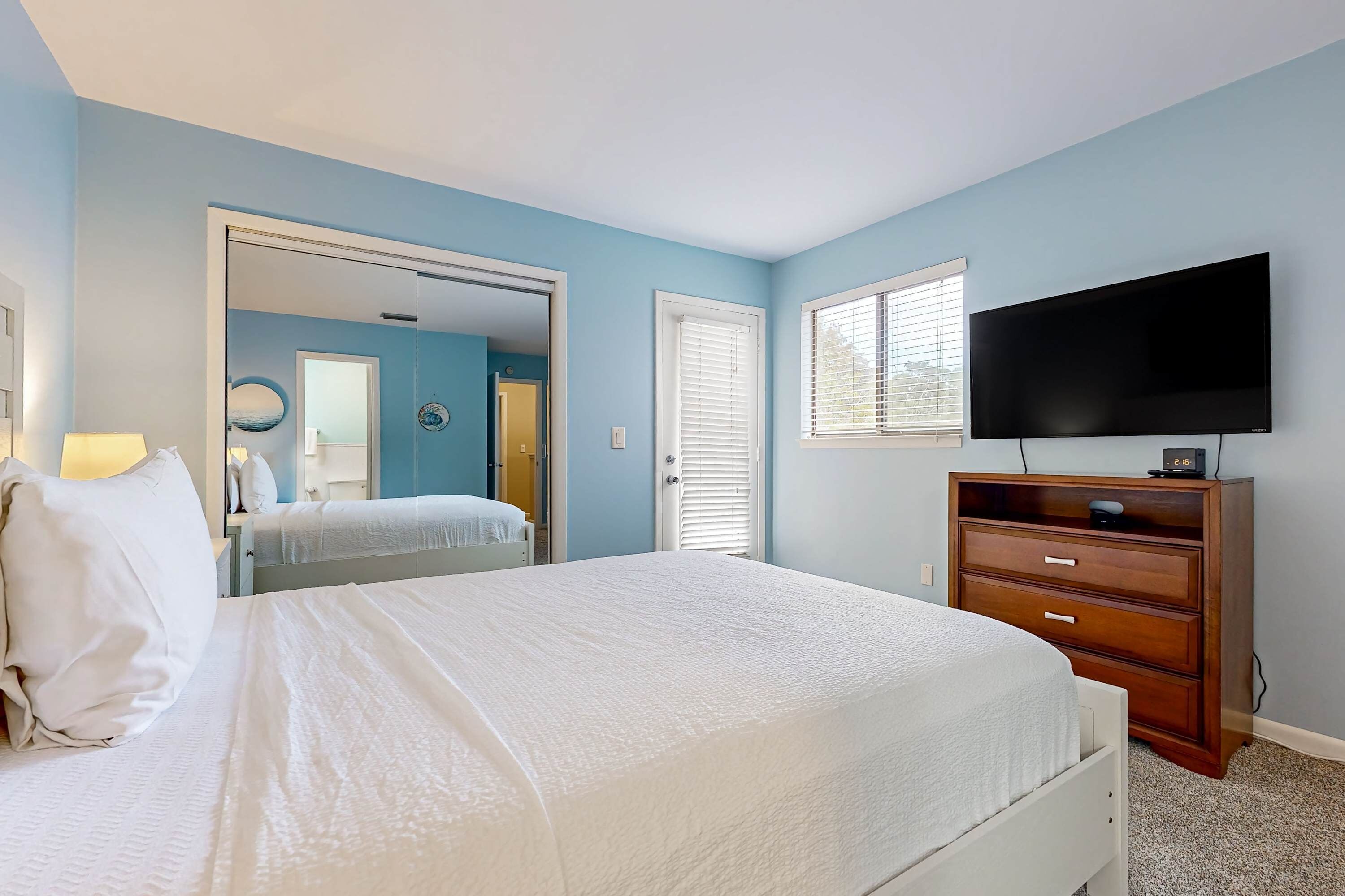 A bedroom with a bed, dresser, TV, and a door leading to another room.