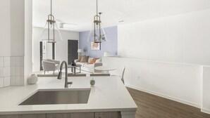 Een moderne keuken met een centraal kookeiland, twee hanglampen en een eethoek met een witte tafel en stoelen.
