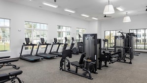 Een fitnessruimte met loopbanden, krachtapparaten en een plafondventilator.