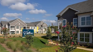 Een wooncomplex met meerdere twee verdiepingen tellende huizen, een centraal bord met 'The Collier' en keurig onderhouden gazons en bloembedden.