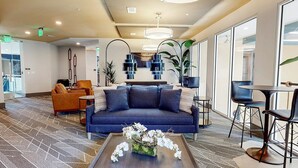 A modern lobby with a blue sofa, orange chairs, a coffee table with flowers, and a large window with a view. - Landing | Spectacular 1BD, Courtyard, Clubhouse (Decatur)