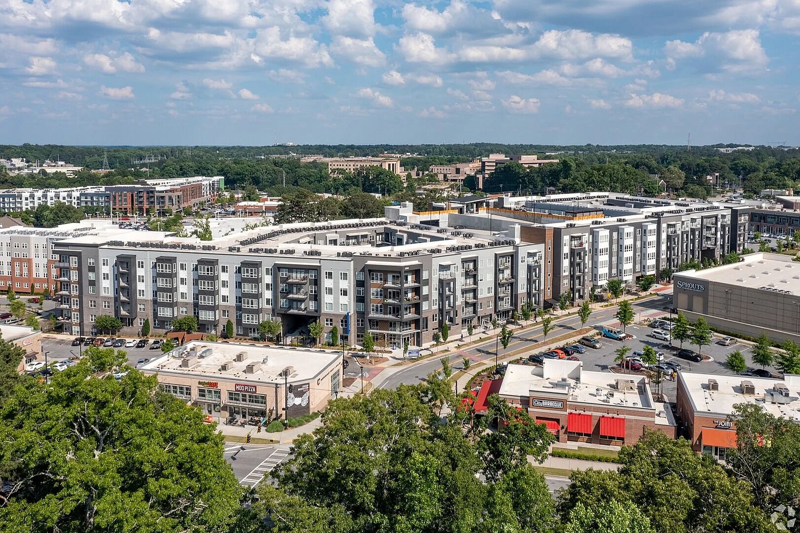 A modern apartment complex with multiple buildings, a parking lot, and surrounding greenery.