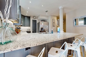 A modern kitchen with a granite countertop, stainless steel appliances, and bar seating. - Private beach access, tennis retreat, 8 guests (Miramar Beach)