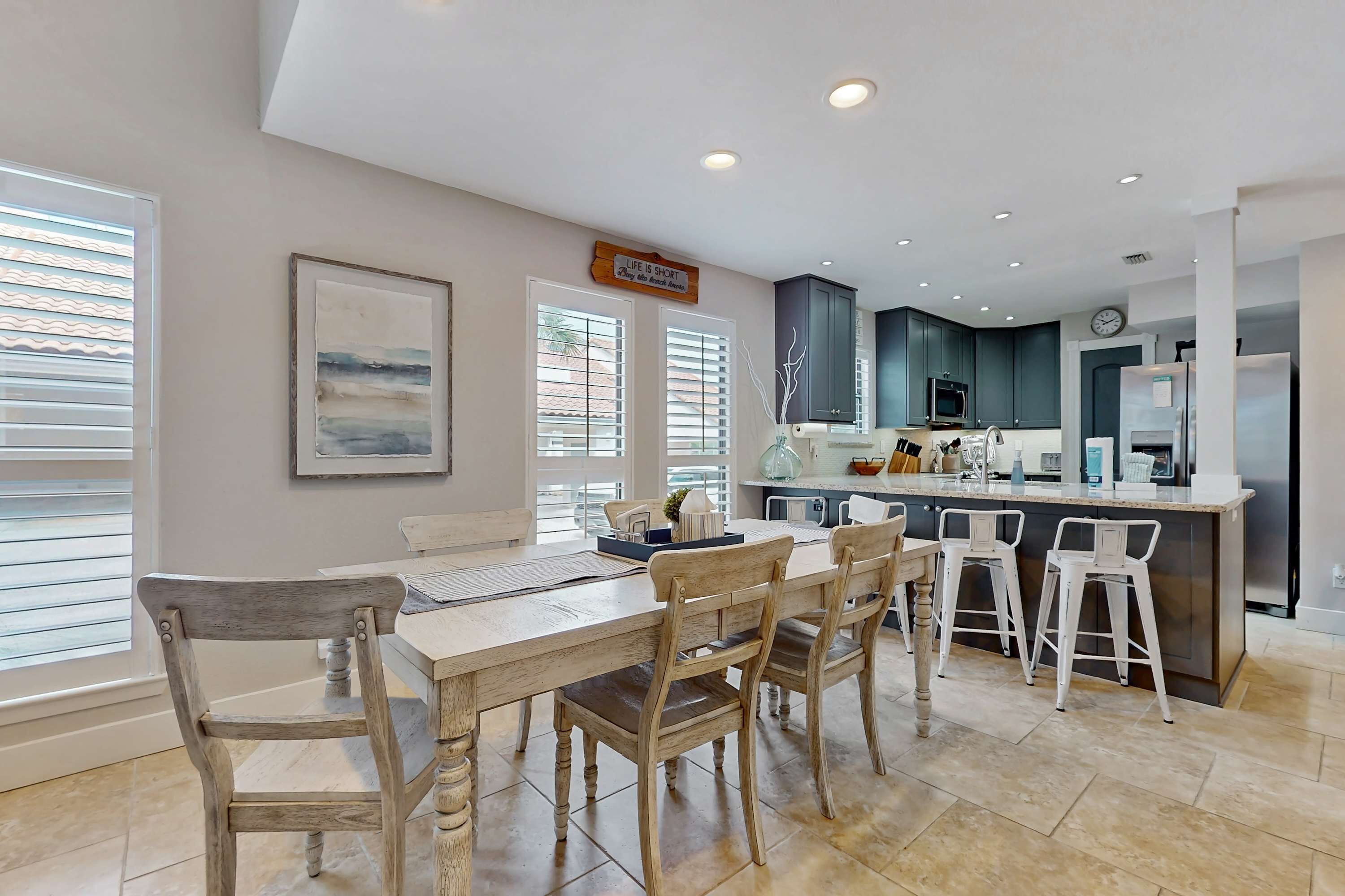 A modern kitchen with dark cabinets, a central island, and a dining area with wooden chairs.