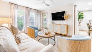 Ein Wohnzimmer mit Sofa, Sessel, Couchtisch, Fernseher und Deckenventilator.