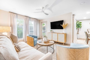 A living room with a sofa, armchair, coffee table, TV, and a ceiling fan. - Exclusive 2BR condo, steps to beach & pool (Miramar Beach)