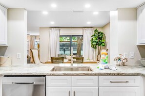 A modern kitchen with a built-in dishwasher, a large sink, and a dining area with a table and chairs. - Exclusive 2BR condo, steps to beach & pool (Miramar Beach)