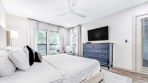 Ein Schlafzimmer mit Bett, Kommode, Fernseher und einem Fenster mit Vorhängen.