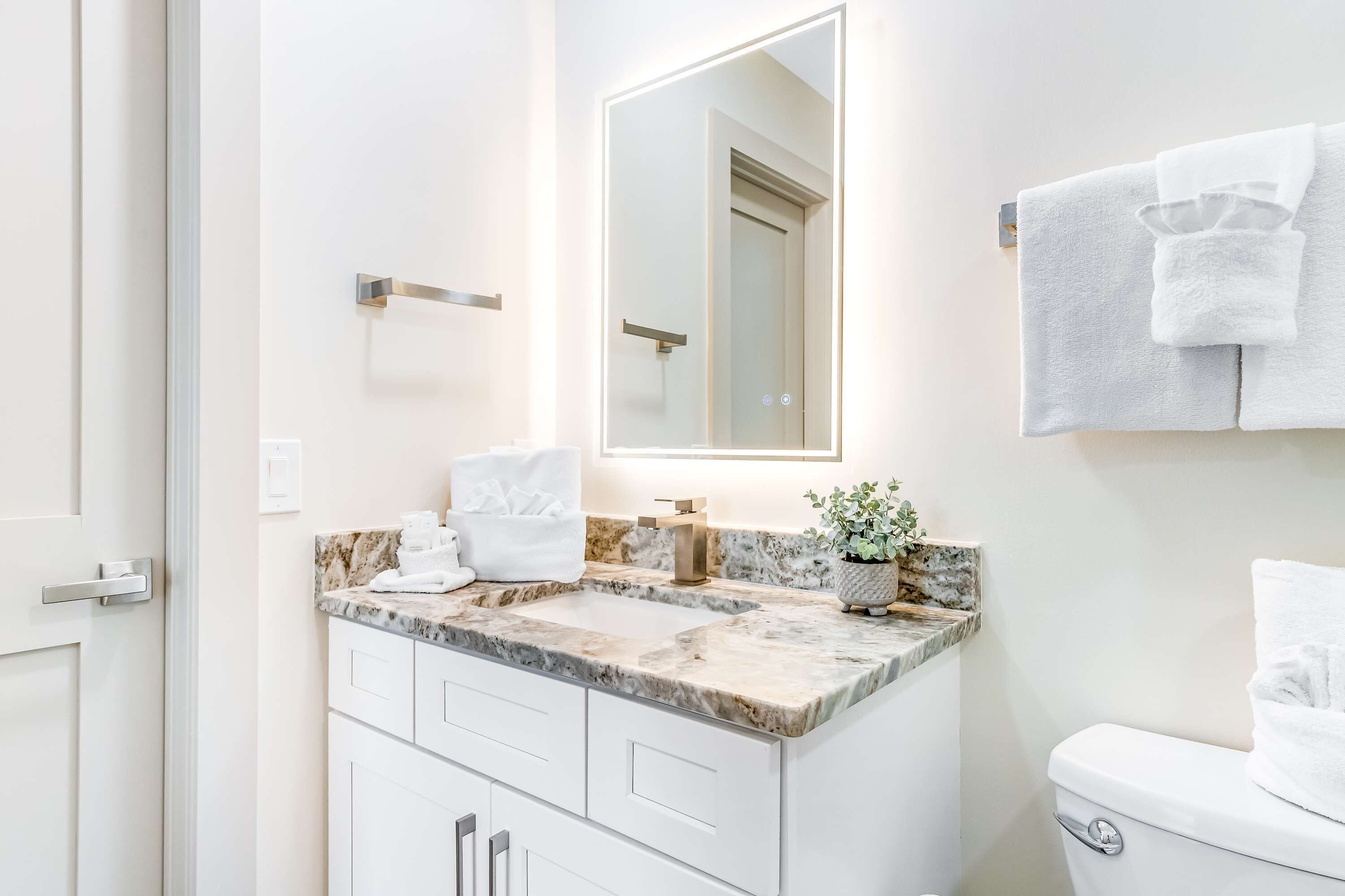 A bathroom with a marble countertop, a mirror, a toilet, and a towel rack.