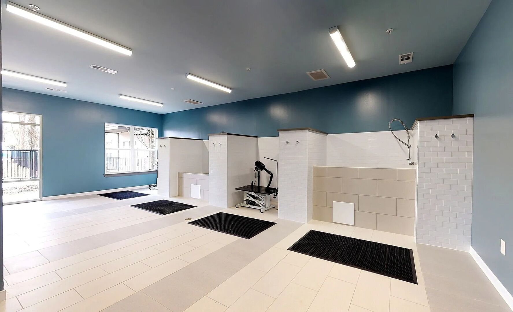 Ein modernes Badezimmer mit weißen und beigen Fliesen, einem schwarzen Trainingsgerät und einem großen Fenster mit Außenblick.