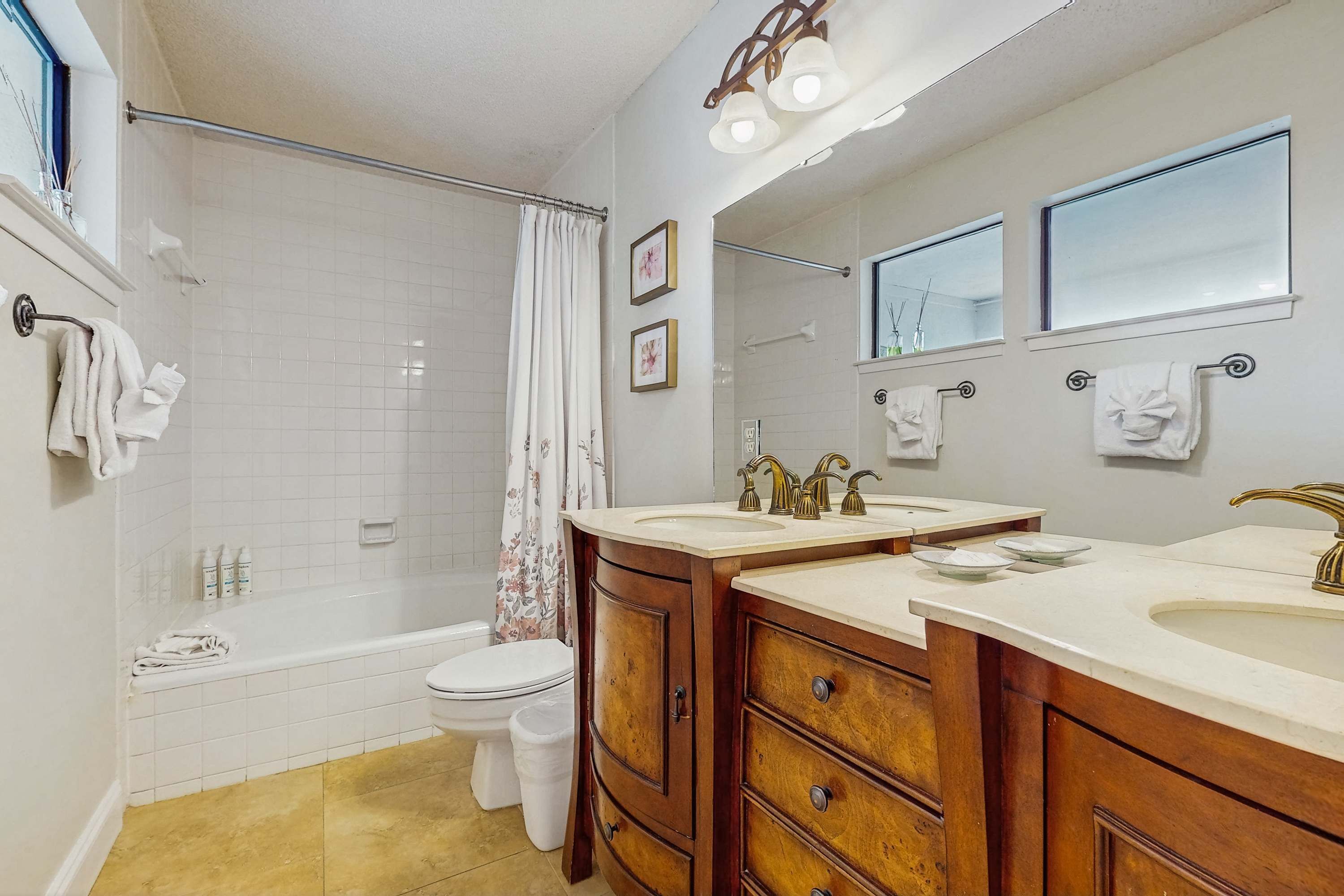 A bathroom with a bathtub, two sinks, a toilet, and a shower curtain.