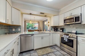 A modern kitchen with stainless steel appliances, white cabinetry, and a large island with a dishwasher. - Exclusive 2BR condo: Pool, tennis, beach access (Miramar Beach)