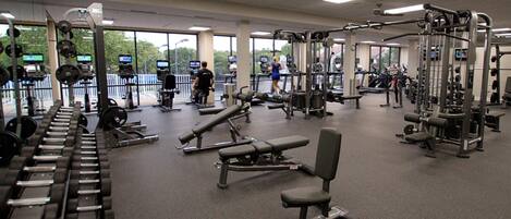 A gym with various exercise equipment, large windows, and a view of the outside.