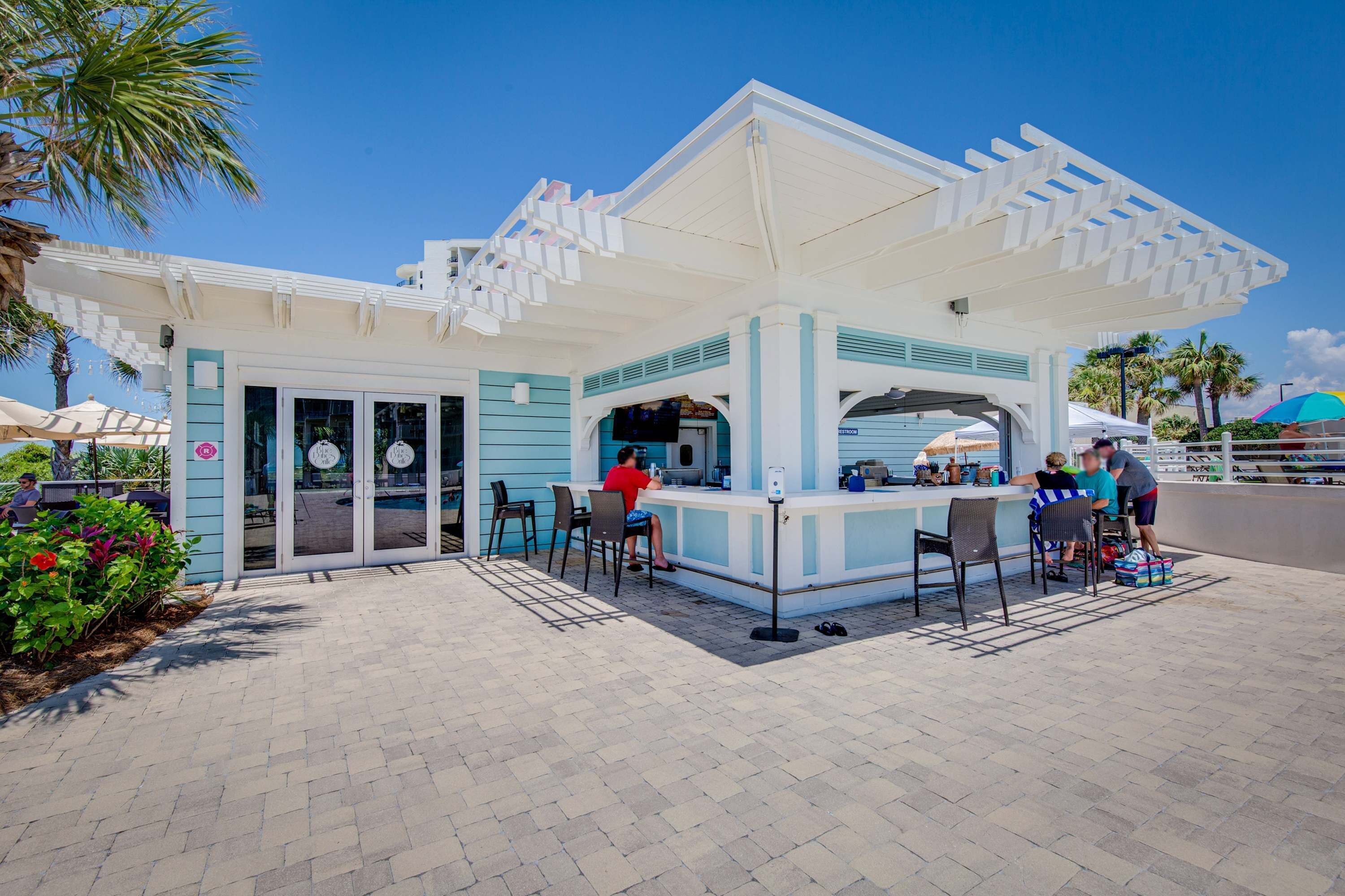 A beachside kiosk with a white and blue color scheme, outdoor seating, and a sheltered area.