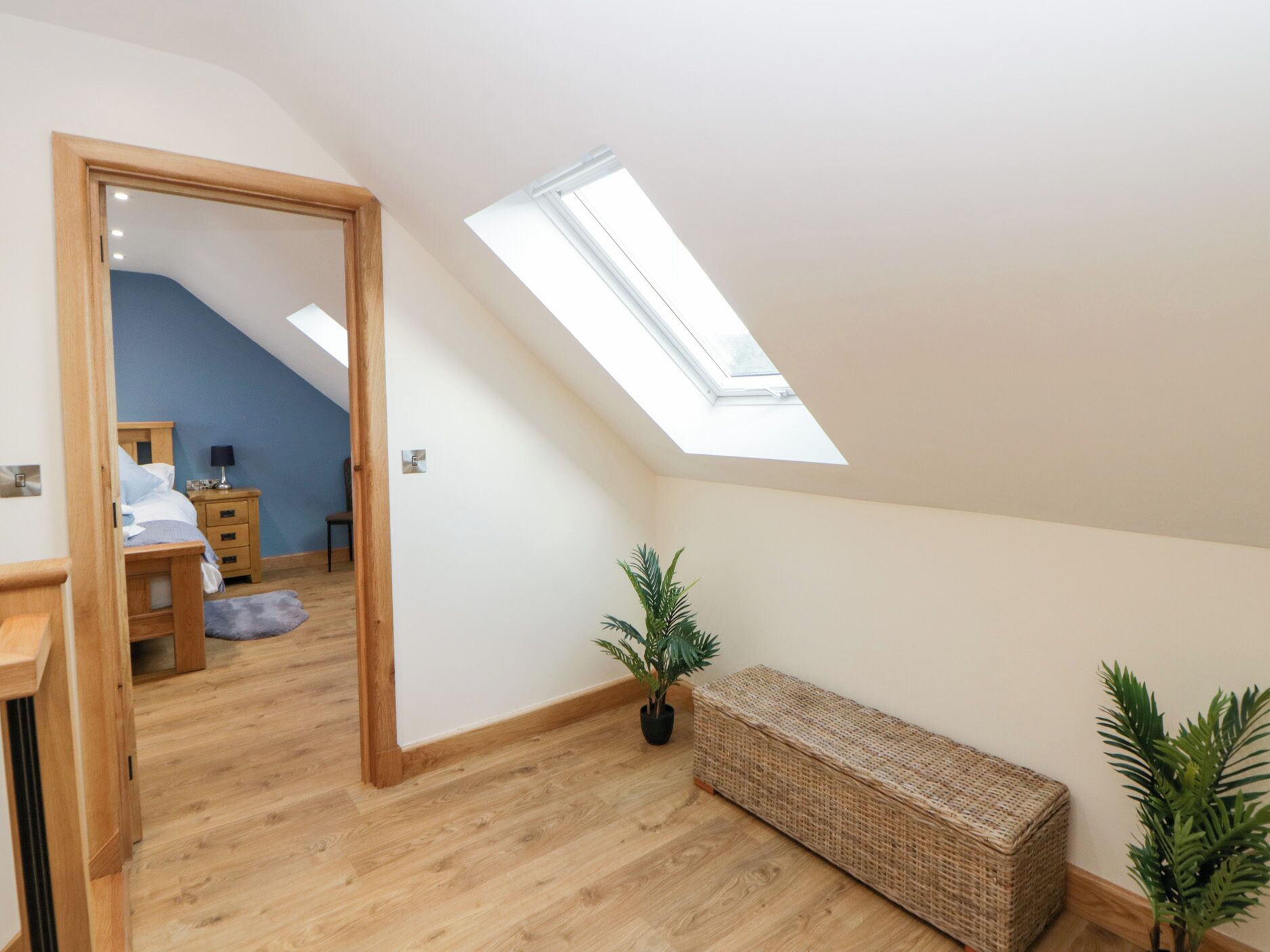 A bedroom with a skylight, wooden flooring, a bed, a nightstand, and a bench.