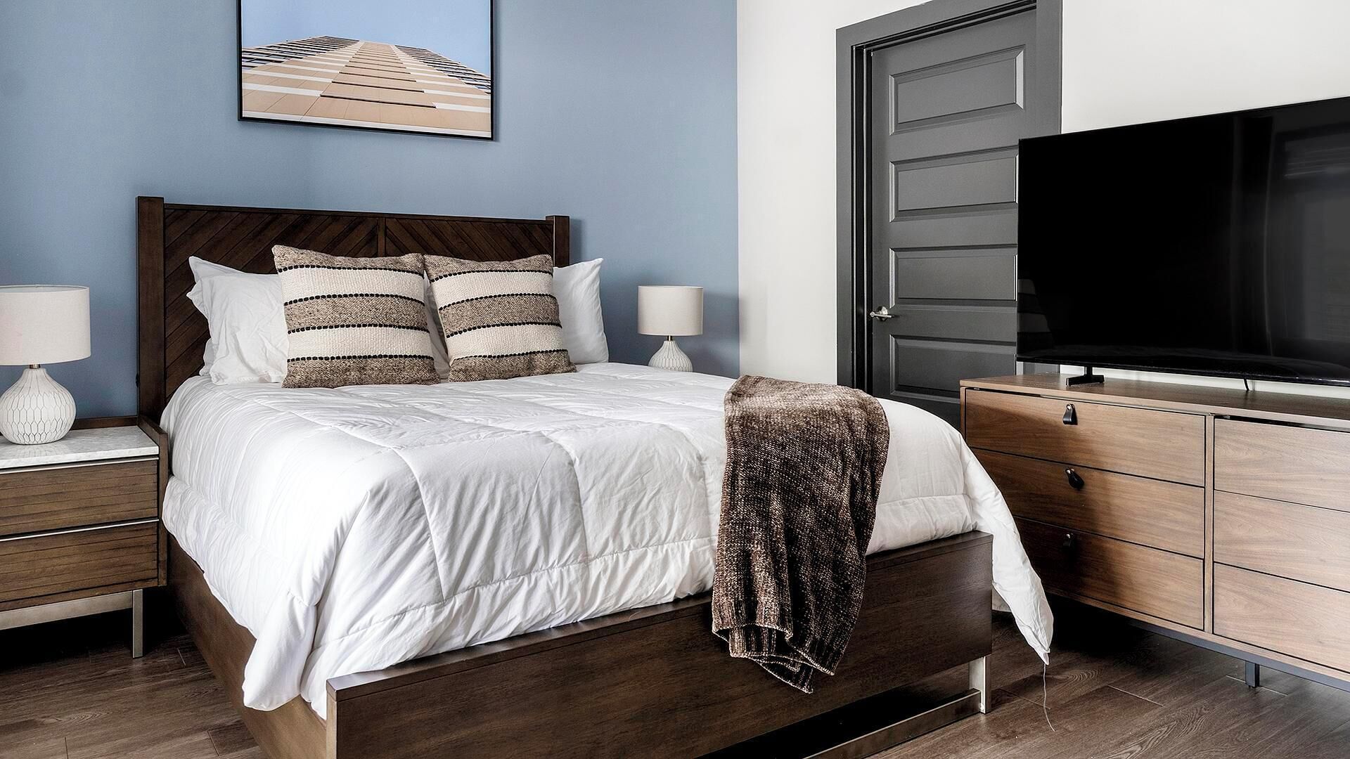 A bedroom with a bed, nightstands, a dresser, a television, and a framed picture on the wall.