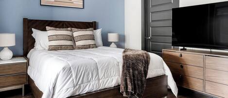 A bedroom with a bed, nightstands, a dresser, a television, and a framed picture on the wall.