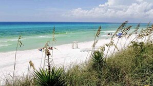Ein Strand mit klarem türkisblauem Wasser, weißem Sand und vereinzelter Vegetation.