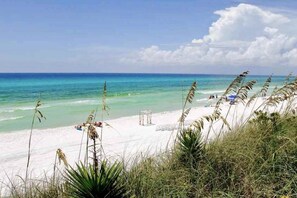 A beach with clear turquoise water, white sand, and sparse vegetation. - Exclusive 2BR: Beach, Pool & Tennis (Miramar Beach)