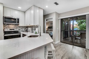 A modern kitchen with a large island, stainless steel appliances, and a sliding glass door leading to an outdoor area. - Exclusive 2BR: Beach, Pool & Tennis (Miramar Beach)