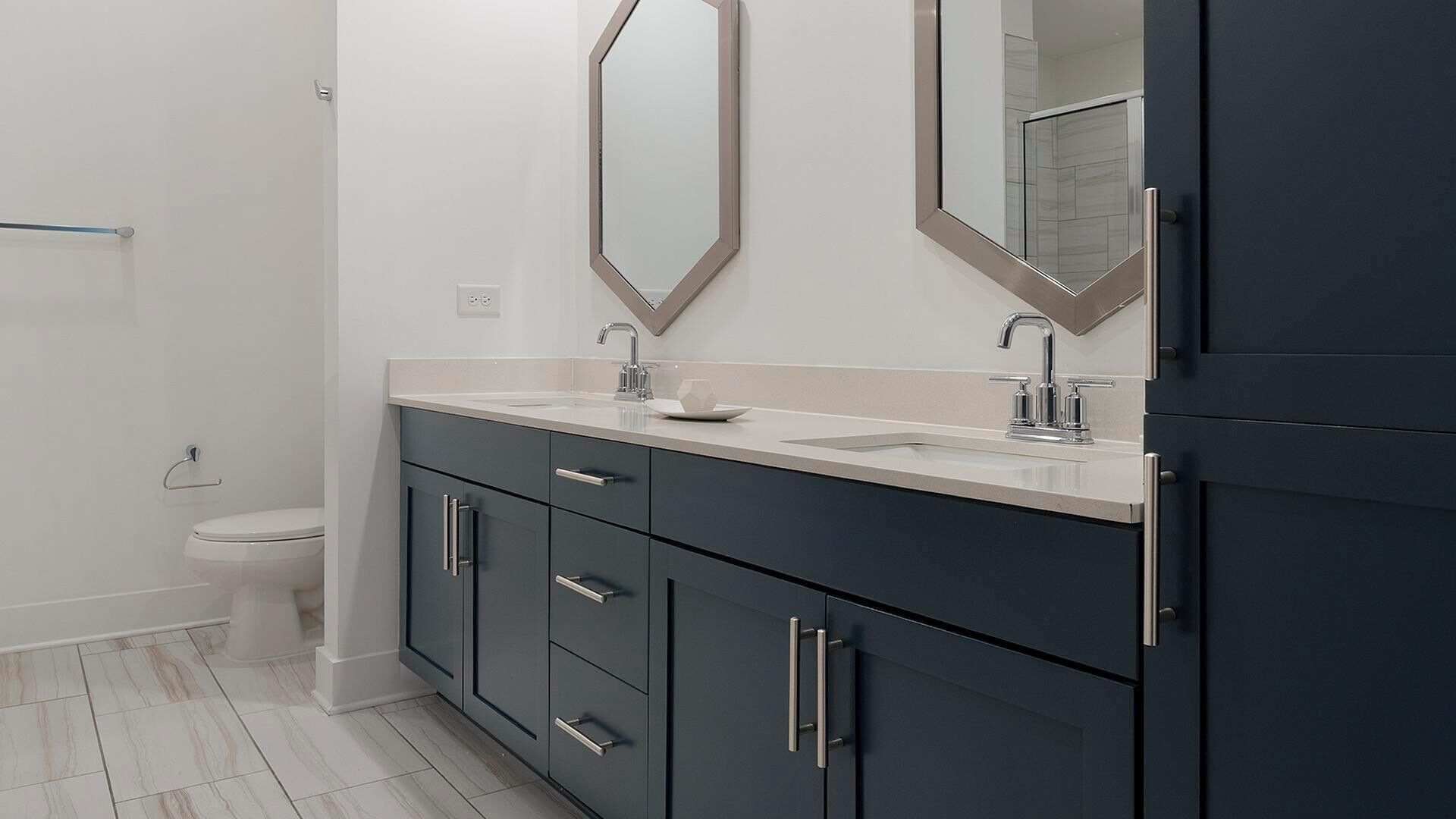 A modern bathroom with a dark vanity, a white sink, and a large mirror.