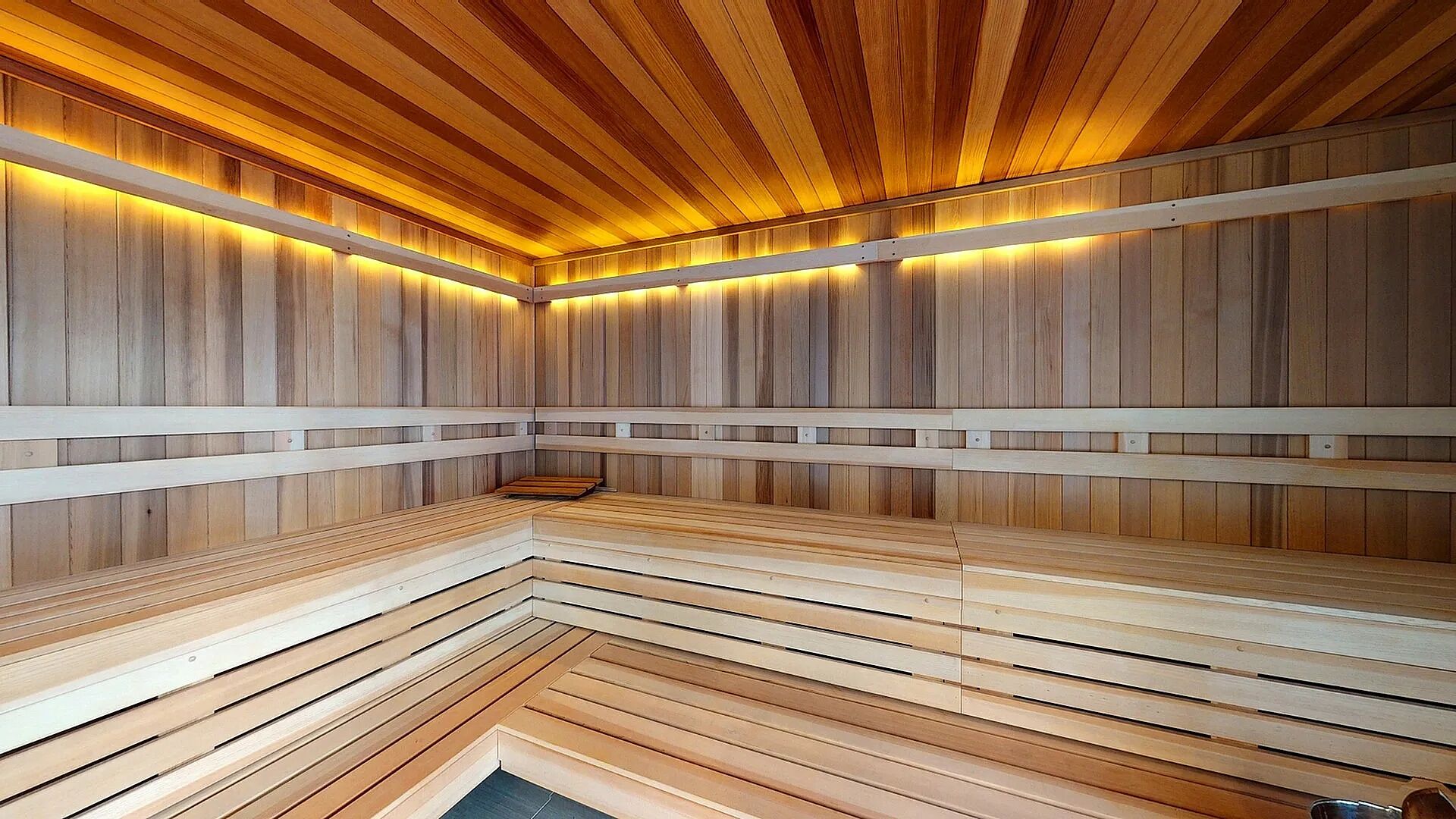 A sauna with wooden slats and a bench, featuring a warm light strip along the ceiling.