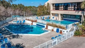 Ein Poolbereich mit mehreren Pools, Liegestühlen und einem Gebäude mit großen Fenstern.
