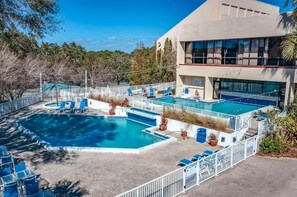 A pool area with multiple pools, lounge chairs, and a building with large windows. - 2BR villa: steps to beach & tennis courts (Miramar Beach)