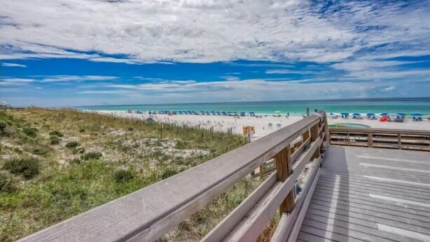 Ein Strand mit einer Holzpromenade, feinem Sand und blauem Himmel.
