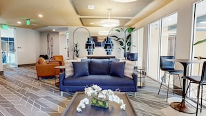 Eine moderne Lobby mit einem blauen Sofa, orangenen Sesseln, einem Couchtisch mit Blumen und einem großen Fenster mit Blick.