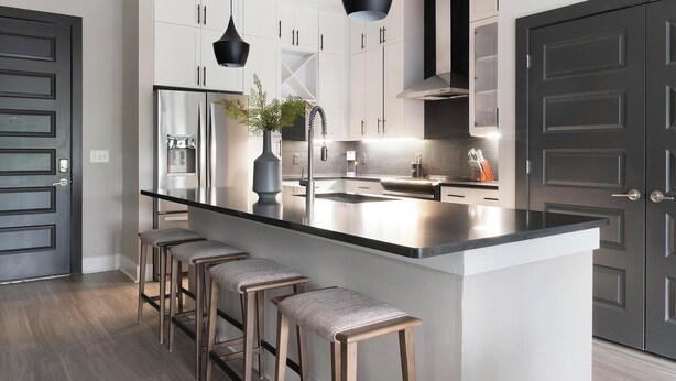 Cozinha moderna com ilha central, banquetas, eletrodomésticos de aço inoxidável e luminária pendente preta.