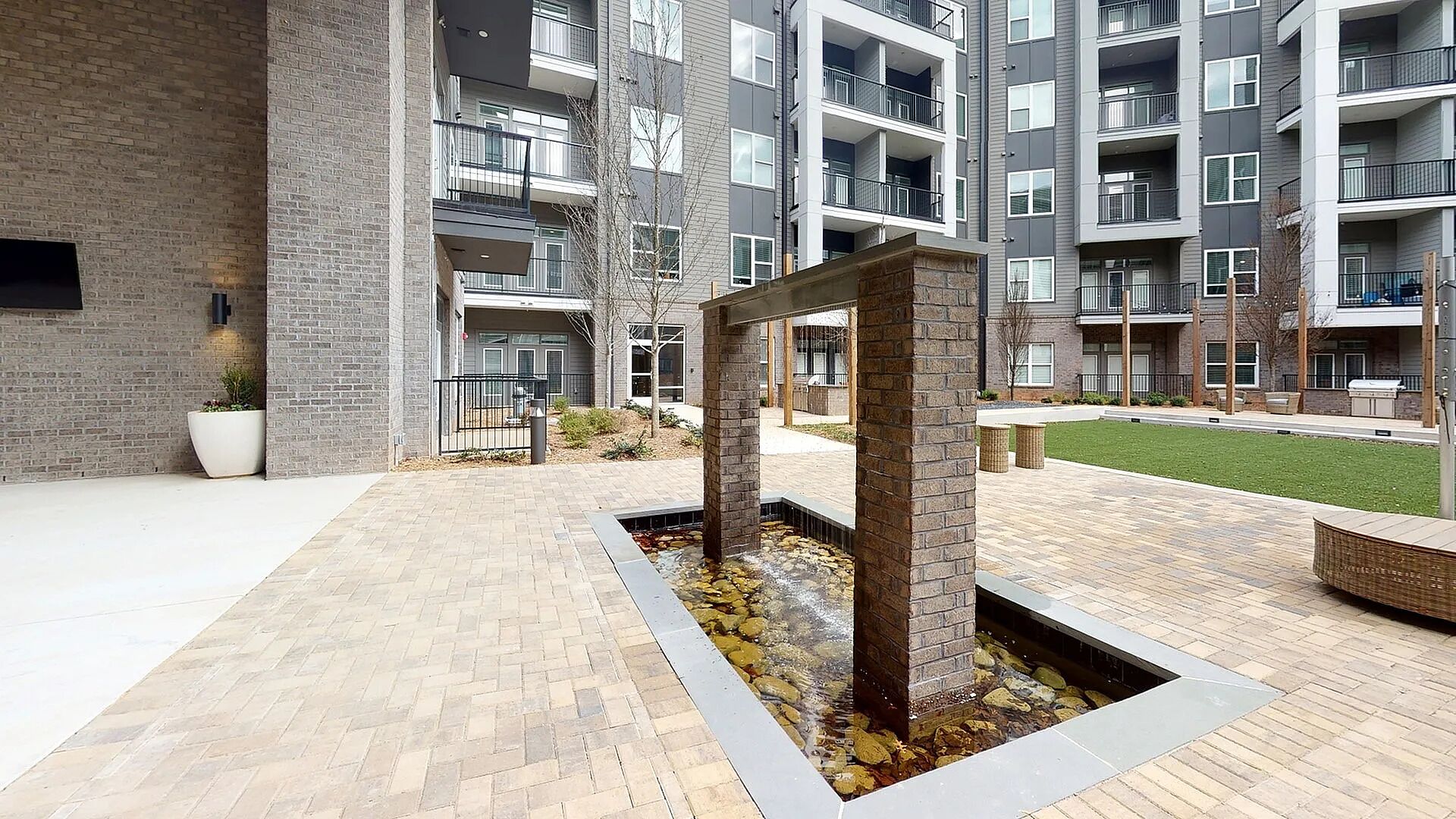 Un immeuble d’appartements moderne doté d’une cour intérieure agrémentée d’une fontaine en pierre, de murs en briques et d’une pelouse bien entretenue.