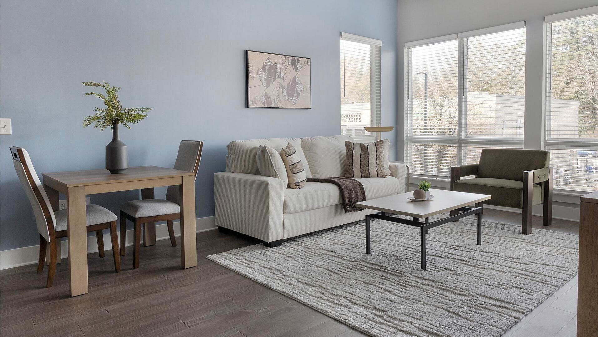 Un salon avec un canapé, une table basse et des fauteuils. On peut voir un vase avec une plante sur la table, et un tableau accroché au mur.
