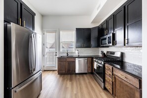 A modern kitchen with dark cabinetry, stainless steel appliances, and a wooden floor.