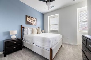 A bedroom with a bed, nightstands, a dresser, a ceiling fan, and a window with blinds. - Landing | Stylish 2BD in Lee's Summit (Lee's Summit)