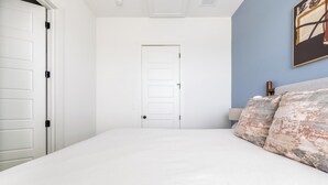A bedroom with a bed, a white door, and a blue wall. - Landing | Modern 2BD in Lee's Summit (Lee's Summit)