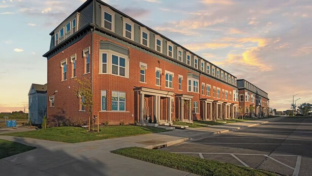 A row of brick townhouses with a garage door entrance, a grassy front yard, and a clear sky. - Landing | Modern 2BD in Lee's Summit (Lee's Summit)