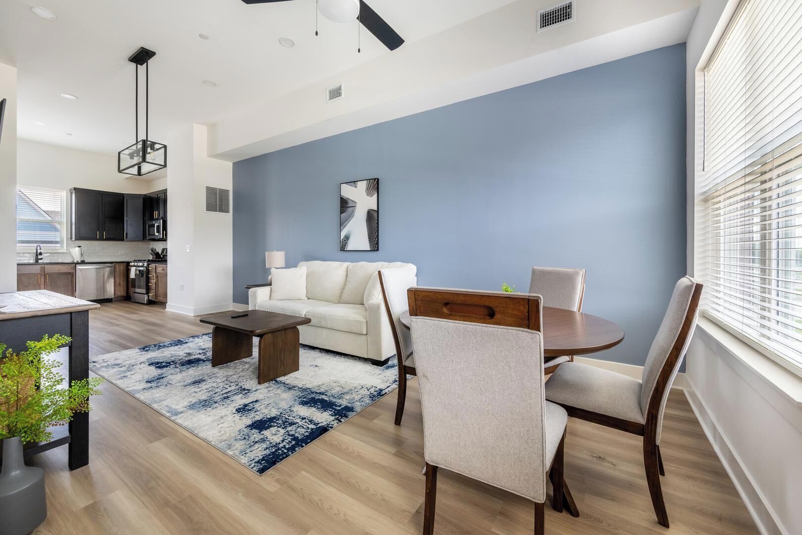 A modern living room with a sofa, coffee table, and dining table. There is a kitchen in the background with cabinets and appliances.