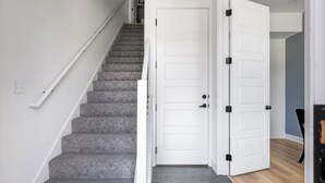 A staircase with carpeted steps leading to a white door with a black handle. - Landing | Modern 2BD in Lee's Summit (Lee's Summit)