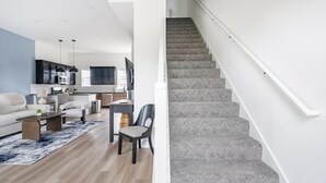 Ein modernes Wohnzimmer mit Sofa, Couchtisch und Essbereich. Eine Treppe mit Geländer ist sichtbar.