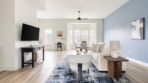 A modern living room with a flat-screen TV, a sofa, a coffee table, and a dining area with chairs and a table. - Landing | Spectacular 3BD in Lee's Summit (Lee's Summit)