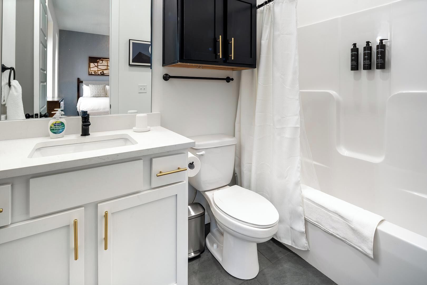 Un bagno con lavandino, water e vasca da bagno bianchi. Sopra il lavandino è presente un mobile contenitore nero e una tenda per la doccia.